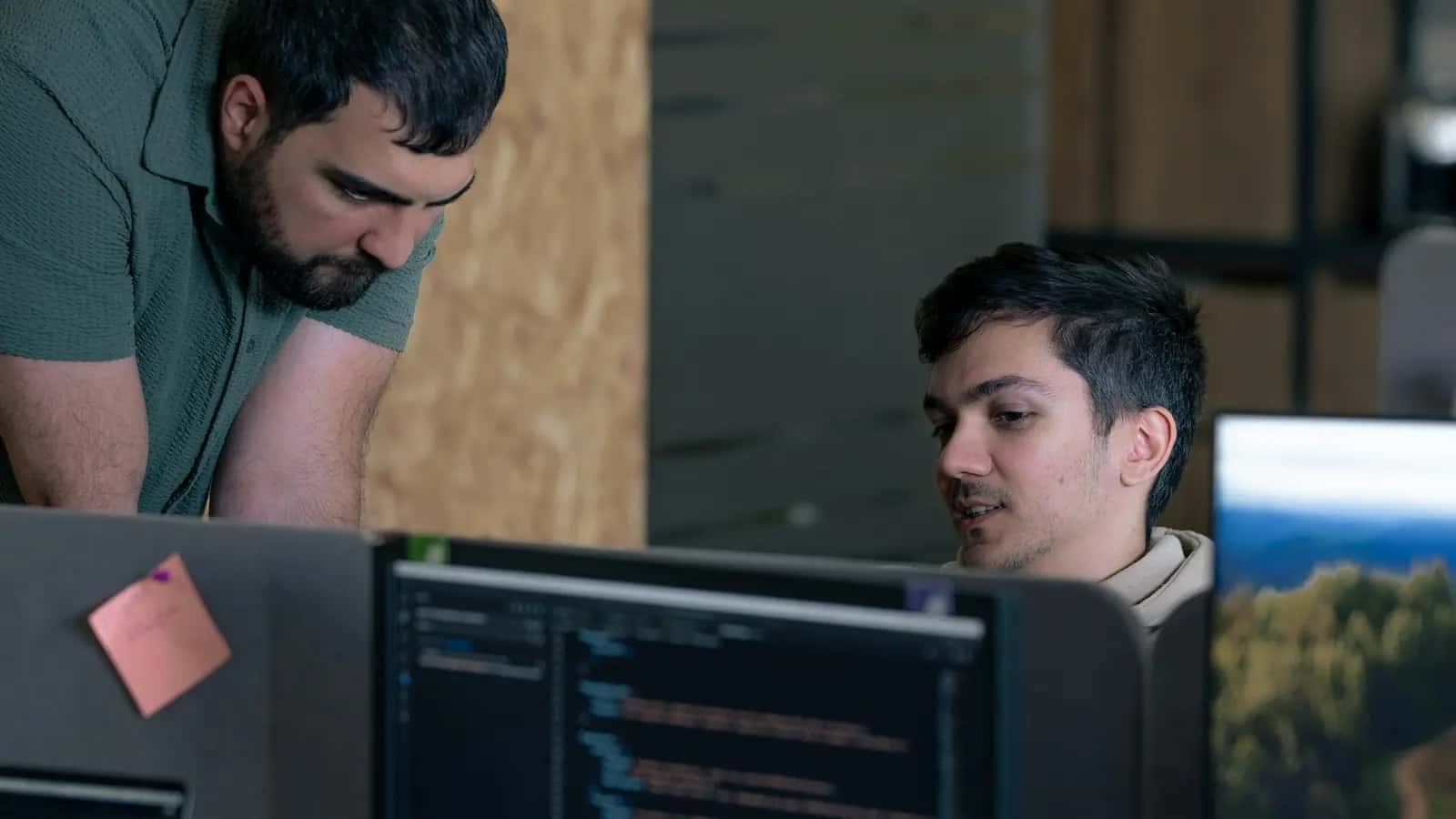 Deux développeurs analysant ensemble du code affiché sur un écran au bureau