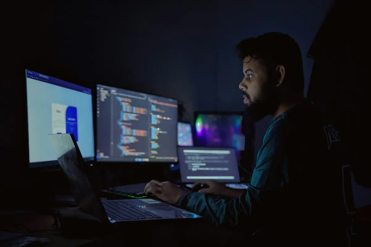 Analyste travaillant de nuit devant plusieurs écrans affichant des données et du code