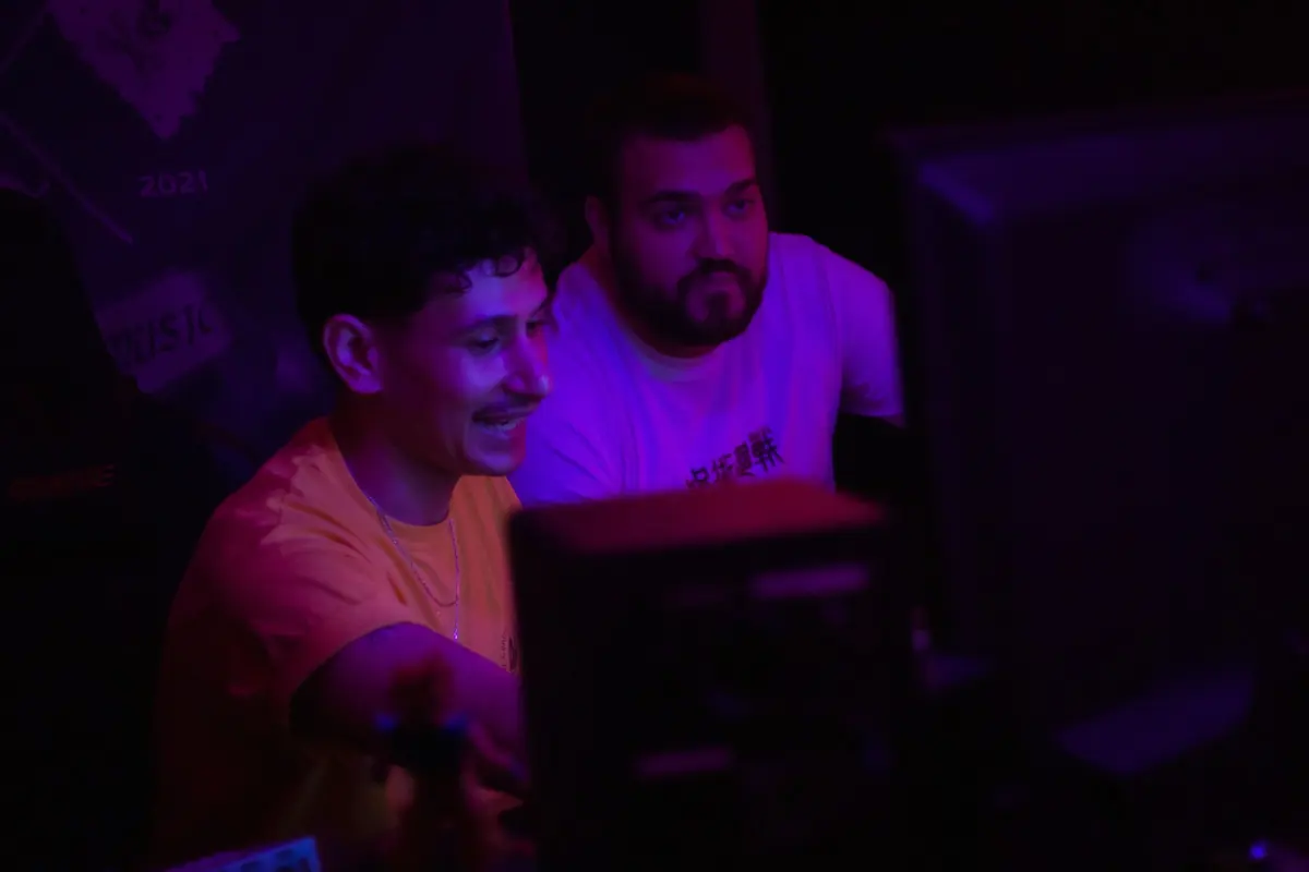 Deux jeunes hommes concentrés devant un ordinateur dans une salle éclairée en violet