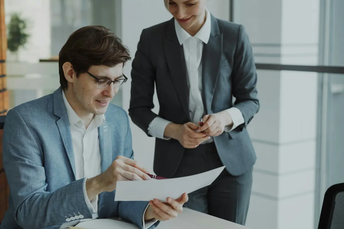 Two colleagues in business suits reviewing a document together in an office