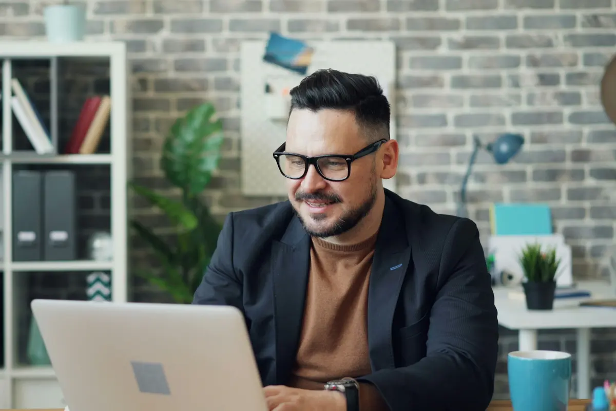 Homme souriant en veste travaillant sur son ordinateur portable dans un bureau