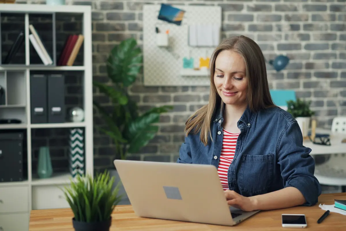 Femme souriante qui apprend sur son ordinateur portable dans un bureau lumineux
